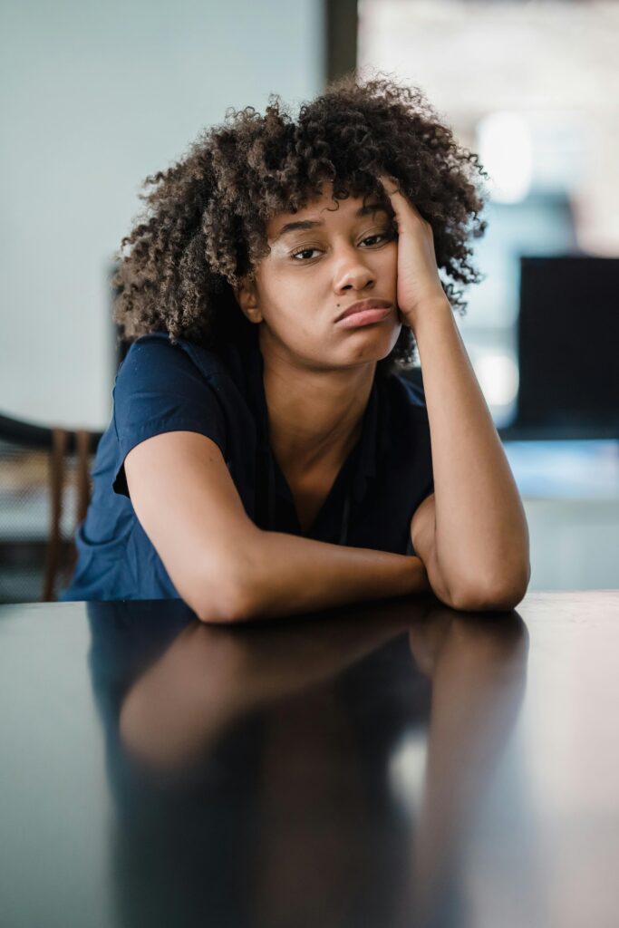 A portrait of a woman looking bored with her head resting on a table indoors.