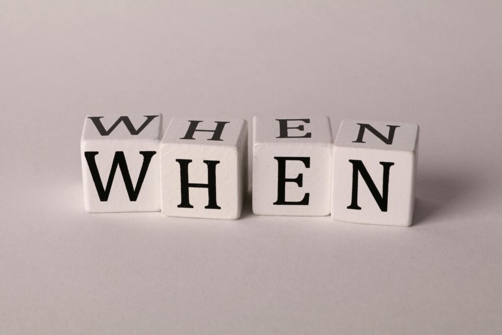 Minimalist photo of wooden blocks with the word 'WHEN' on a white background.