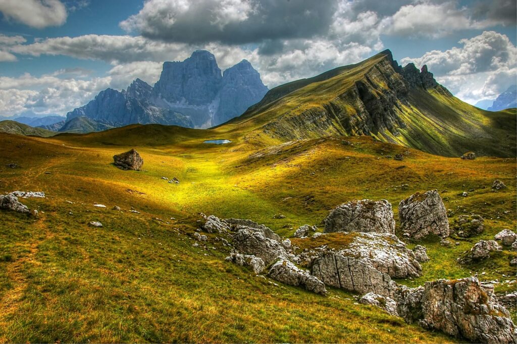 Explore a stunning alpine landscape with rolling hills and majestic mountains under a cloudy sky.